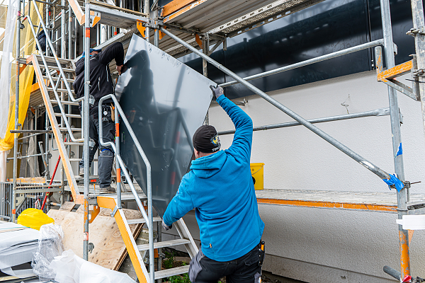 Arbeiter tragen einen Kollektor der solaraktivierten Fassade auf das Gerüst.