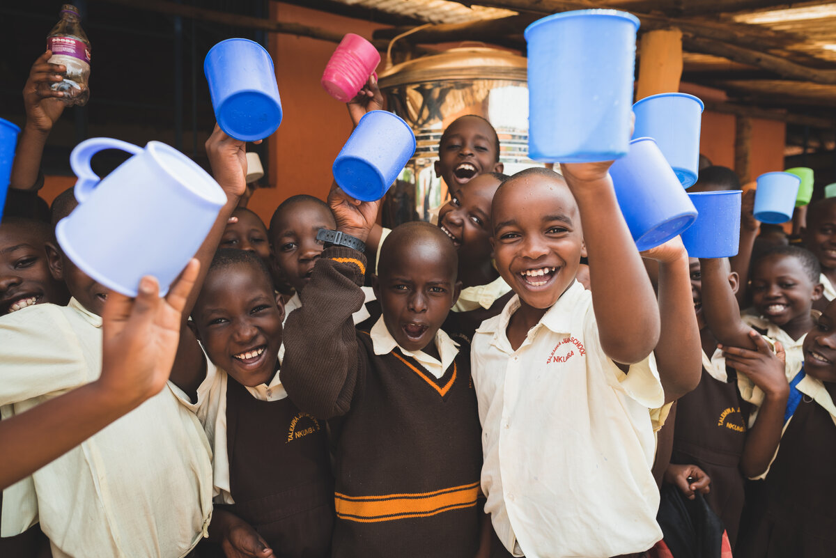 Kinder in Ugandas Hauptstadt Kampala halten Trinkbecher in die Höhe.